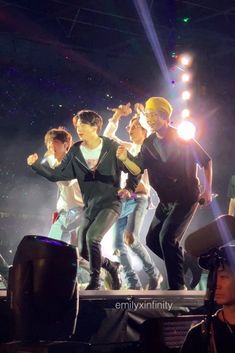 group of young men performing on stage in front of audience at concert with lights behind them