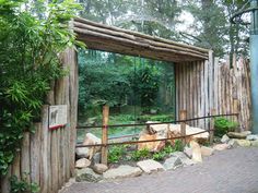 a wooden structure in the middle of a park with trees and rocks surrounding it, surrounded by greenery