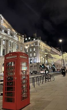 a red phone booth sitting on the side of a road next to tall buildings at night