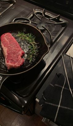 a piece of meat is cooking in a skillet on the stove top with some herbs