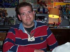 a man sitting at a table in front of a lamp and bookshelf with comics on the wall behind him