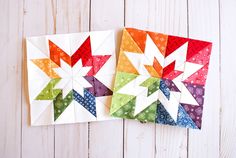 two colorful quilts sitting next to each other on top of a wooden table with white boards