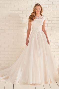 a woman in a white wedding dress standing against a brick wall