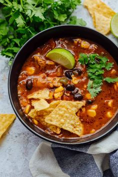 a black bowl filled with tortilla soup next to cilantro and lime wedges