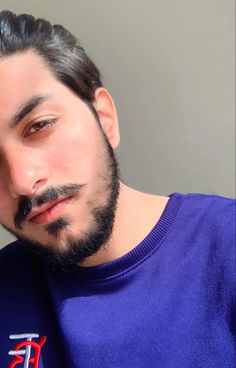 a close up of a person wearing a blue shirt with a beard and moustache