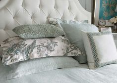 a white headboard with many pillows on it and a clock in the corner next to it