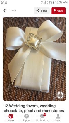 a white gift box wrapped in satin ribbon with a bow and jewel embellishment