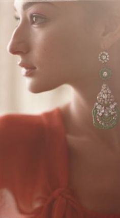 a woman in a red dress with earrings on her head looking off into the distance