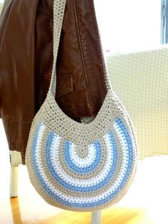 a crocheted bag sitting on top of a wooden table next to a brown leather jacket