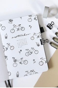 an open notebook with bicycle drawings on it and some pens in front of the pages