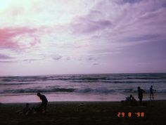 some people on the beach and one is holding a surfboard while others stand in the water