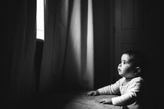 a black and white photo of a baby looking out the window