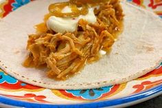 a tortilla with shredded meat and sour cream sits on a colorful floral plate