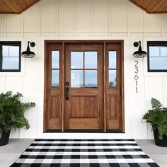 a black and white checkered rug in front of a wooden door with two potted plants