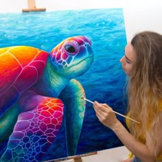 a woman is painting a colorful turtle on the easel while holding a paintbrush