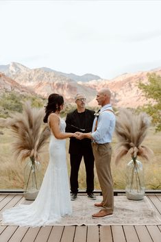 a bride and groom holding hands during their wedding ceremony in front of the desert mountains