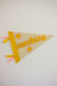 a white and yellow pennant with the word sunshine hanging on it's side against a wall