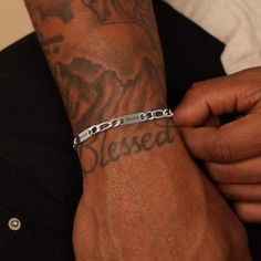 a man wearing a silver bracelet with the word messed on it's wrist and holding onto his arm