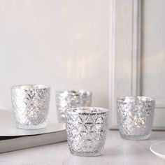 three silver glass cups sitting on top of a table next to a book and plate