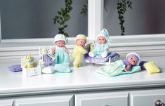 three dolls are sitting on a table with their babies in crocheted blankets and hats