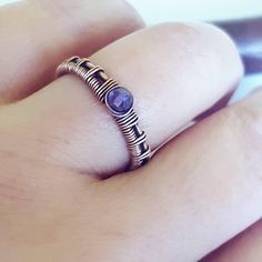 a person's hand holding a ring with a purple stone in the middle and silver wire around it