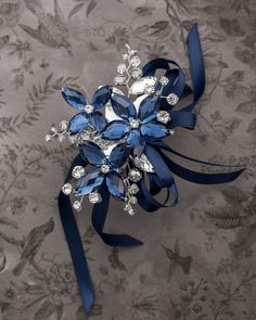 a brooch with blue ribbon and crystal stones on it's side, sitting on a floral wallpapered surface