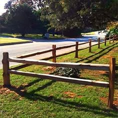 a wooden fence in the middle of a grassy area next to a road and trees