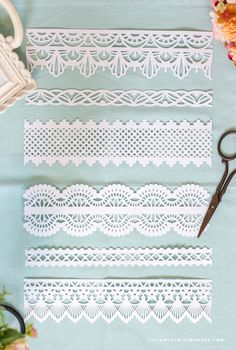 white crochet laces and scissors on a blue tablecloth with pink flowers