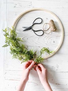 two hands are holding plants in front of an embroidery hoop with scissors and yarn on it