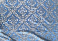 a blue and silver brocaded fabric with white flowers on it's edges