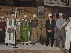 a group of men standing next to each other in front of a brick wall with a cross on it