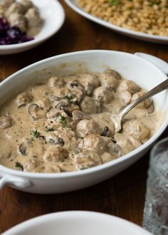 a white bowl filled with meatballs and gravy on top of a wooden table