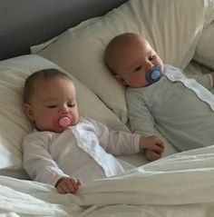 two babies laying in bed with pacifiers on their mouths