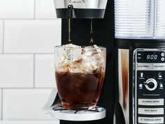 an iced drink being poured into a glass in front of a coffee maker on a counter