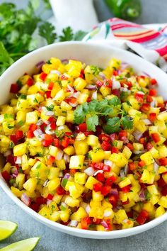 a white bowl filled with pineapple salsa next to cilantro and lime wedges