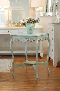 a white table with a vase on top of it in front of a dresser and mirror