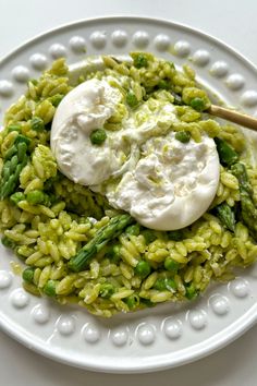 a white plate topped with green pasta and asparagus next to sour cream on top