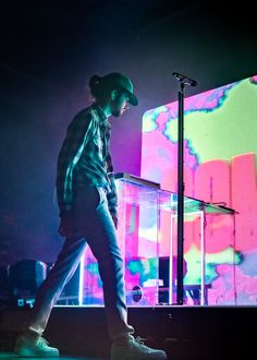 a young man walking across a stage in front of a colorful light display on the wall