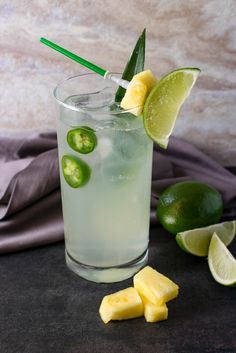 a glass filled with ice and limes on top of a table next to sliced pineapple