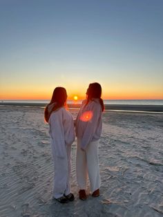 two women standing on the beach at sunset