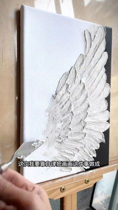 someone is painting an angel wing with white paint on the canvas, and it looks like they are flying