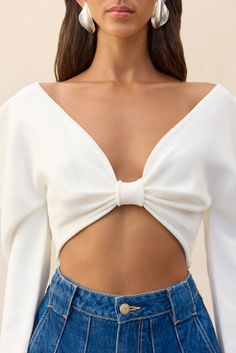 A long sleeve knit crop top with a plunging neckline and exaggerated shoulders. — Plunging neckline — Cropped length — Long sleeves that can be worn on the shoulder or regularly — Cinched at bust White Fitted V-neck Cropped Sweater, Chic White V-neck Crop Top, Chic Summer Cropped Sweater, V-neck Crop Top For Brunch In Fall, Chic Low-cut Crop Top For Spring, Fall V-neck Crop Top For Brunch, Long Sleeve Cropped Sweater For Night Out In Spring, Long Sleeve Cropped Sweater For Spring Night Out, Elegant Spring Cropped Sweater