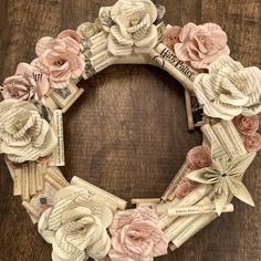 a wreath made out of old book pages with flowers on it, sitting on top of a wooden table