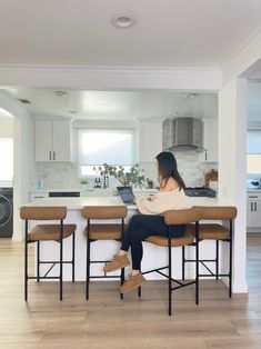 a woman sitting at a kitchen counter using a laptop