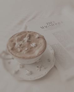 a cappuccino on a saucer next to a magazine with white flowers