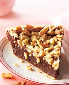 a piece of chocolate pie on a plate with walnuts next to it and a pink napkin