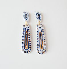 two pairs of blue and orange earrings on a white surface, one with an oval shaped design