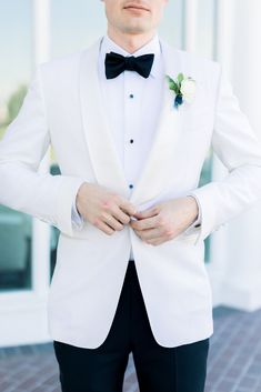 a man in a white tuxedo and black pants stands with his hands on his hips