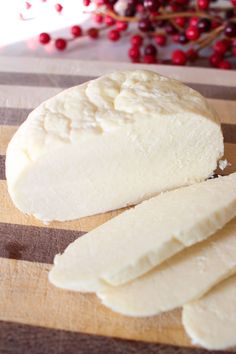 slices of cheese sitting on top of a wooden cutting board next to cranberries