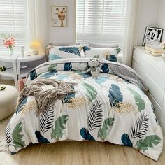 a bed room with a neatly made bed next to a white dresser and window covered in blinds